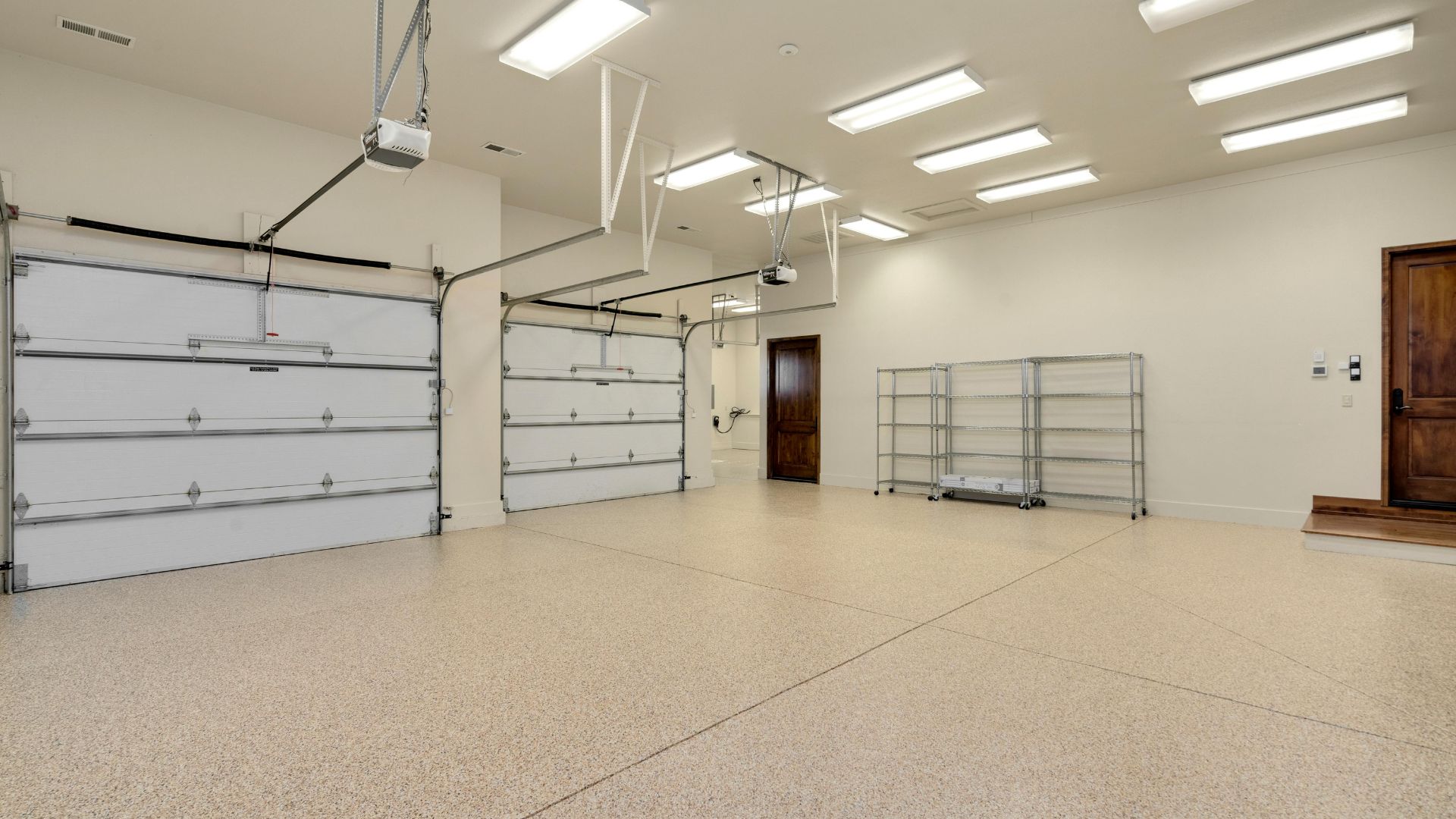 Empty clean garage with white walls, large doors, and metal shelving