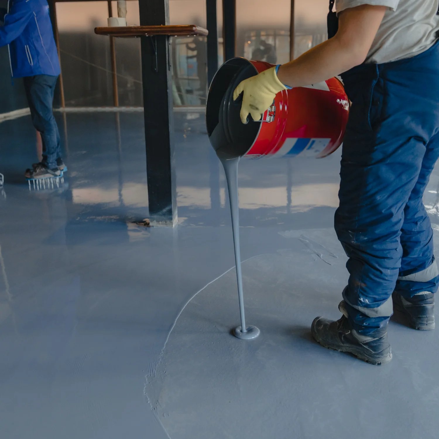 Worker pouring gray epoxy resin on concrete floor during renovation