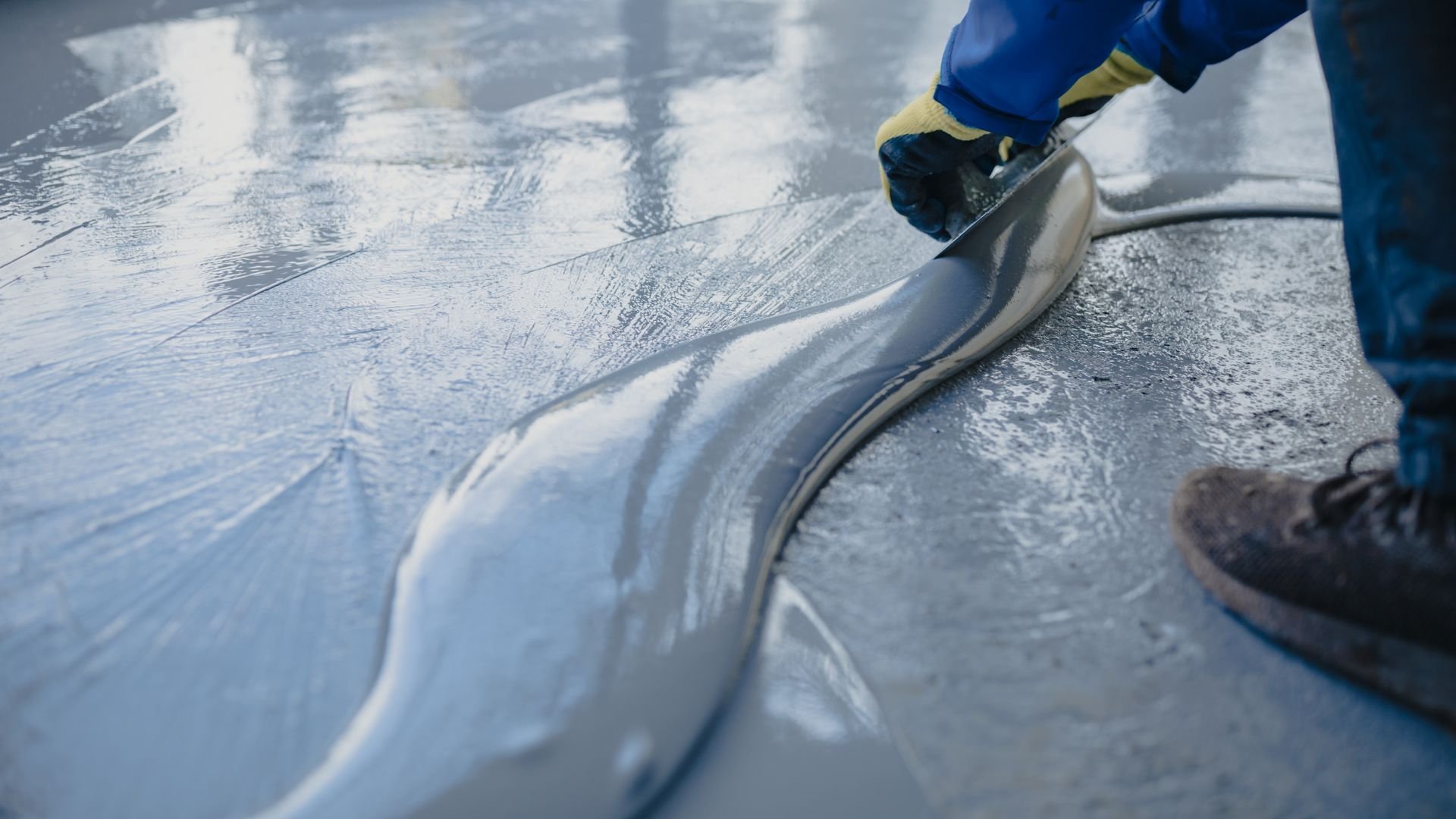 Worker spreading liquid floor coating with squeegee in blue gloves