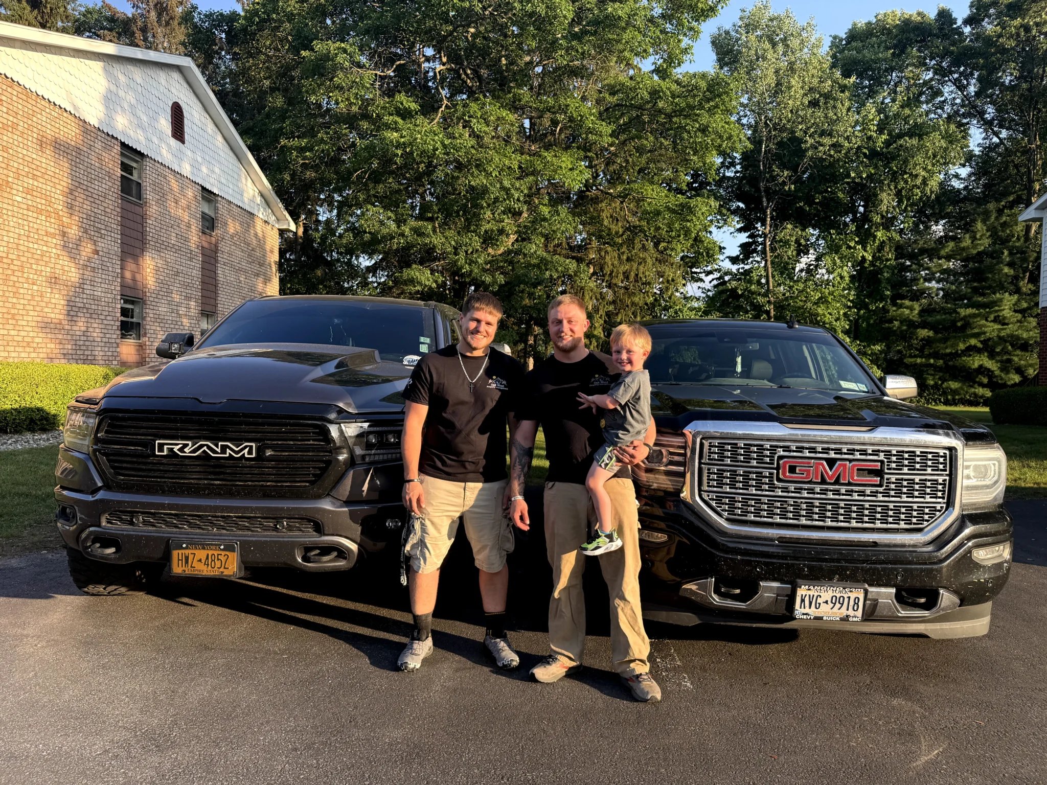 Three people standing between RAM and GMC trucks in residential driveway