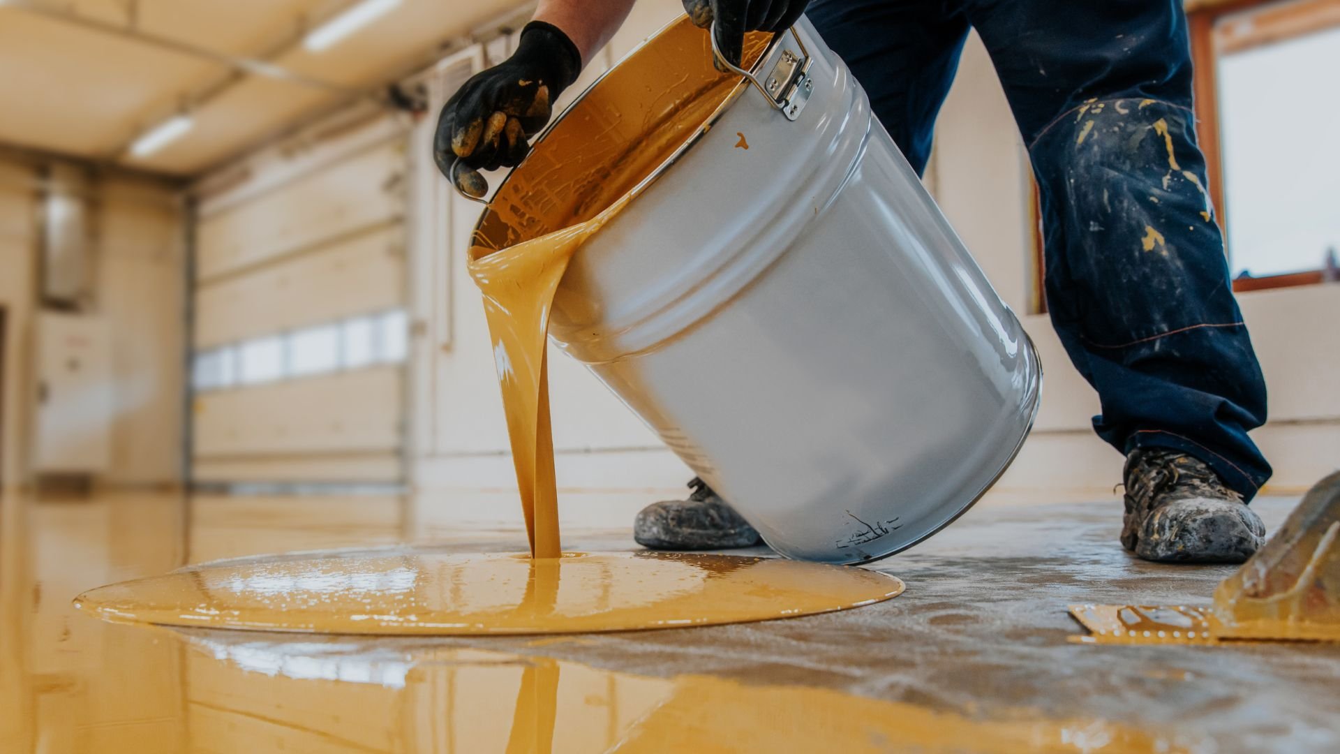 Yellow paint pouring from metal bucket onto floor during renovation
